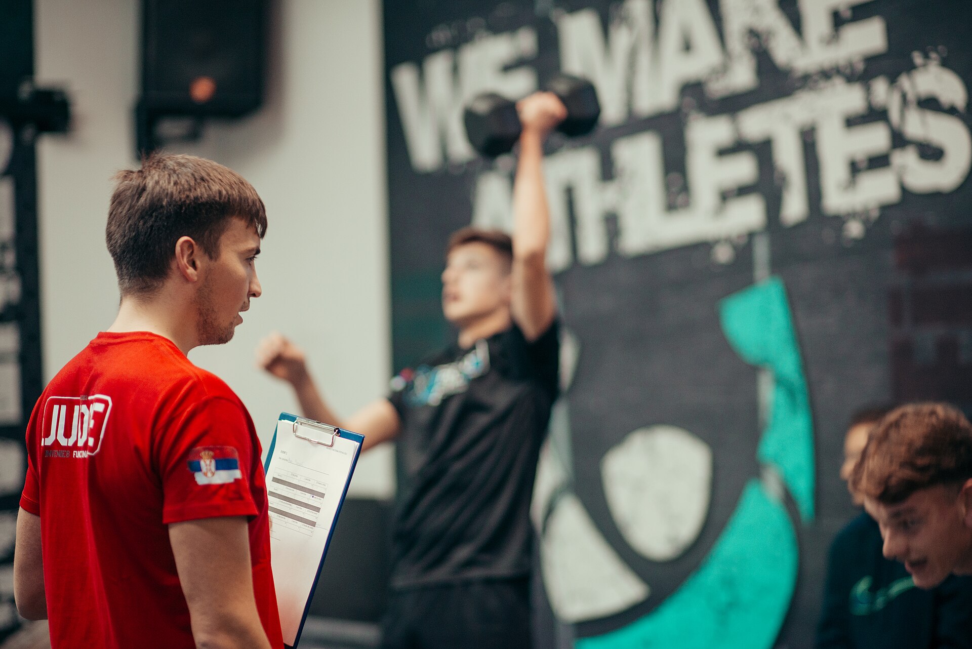 A coach with a clipboard watching an athlete lift